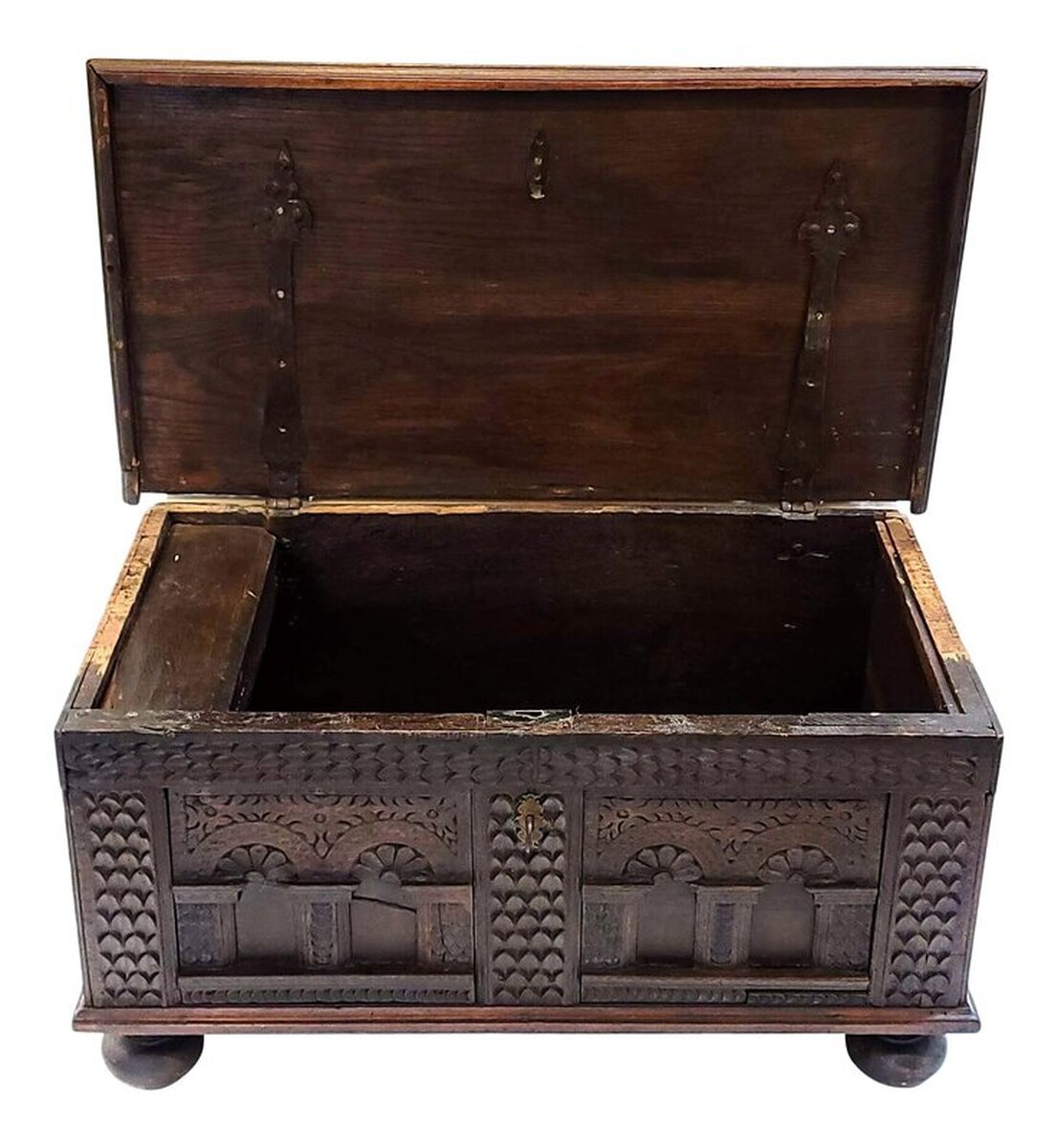 Spanish Renaissance period carved oak arcón with iron and brass mounts.  Antique chest from the 1600s is peg constructed of oak wood.  The lid is solid burl figured oak attached to the carcass with wrought iron diamond tipped strap hinges on the underside.  The front panels show carvings of foliated spandrels over arcading arches cupping floral fans. The arches stand on plinth bases.  The original key fits through a chased brass escutcheon sporting a foliated scroll and lozenge motif.  The carcass rests upon four turned oak bun feet.  The side panels are fitted with twisted wrought iron bail handles. The handles indicate this may have been built for use as a traveling trunk or campaign chest.  The back is of a plain board.  The interior is fitted with a hinged-lid box on the top left side for storage of candles and other small objects.  Outer surfaces are finished with hand rubbed paste wax.