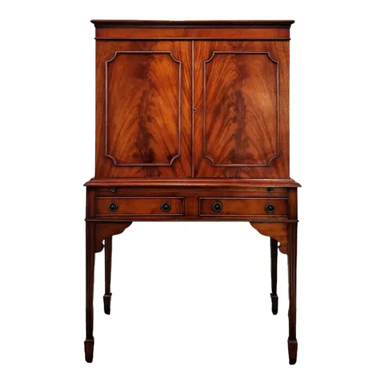 Georgian style mahogany cocktail cabinet was built by Bevan Funnell Ltd., Beach Road, Newhaven, Sussex, England. Bevan Funnel was established in 1945 and is known for bespoke and classically influenced furniture designs.  This drinks cabinet was constructed from mahogany wood in the mid-to-late-20th-century. The top and sides feature ribbon figured mahogany and the door fronts feature flame, or crotch cut, mahogany.  Under the flat top with molded edge is a cabinet with two locking doors lined on the interior with plain sycamore wood. The interior of the cabinet is lined with figured sycamore wood and mirrored on the back and bottom. A light fixture at top turns on when plugged in. The interior also contains a removable shaped sycamore wood shelf.  The cabinet comes with a key.  Below the cabinet is a pull-out shelf for use as a cocktail prep station. The shelf easily slides forward with a pull on the two round brass knobs.  Two frieze drawers are located under the pull-out shelf and may be opened with a tug on the circular ring pulls over round decorative escutcheons.  Curvy supports are placed under the front apron where the front legs attach.  All four legs are square fluted tapers ending in spade feet.  All hardware is solid brass.  This mahogany cocktail cabinet will complement interiors with elements of Georgian, Sheraton, Hepplewhite, Chippendale, Queen Anne, Victorian and Edwardian Sheraton styles.  The cabinet will blend nicely with your Bevan Funnell ranges 