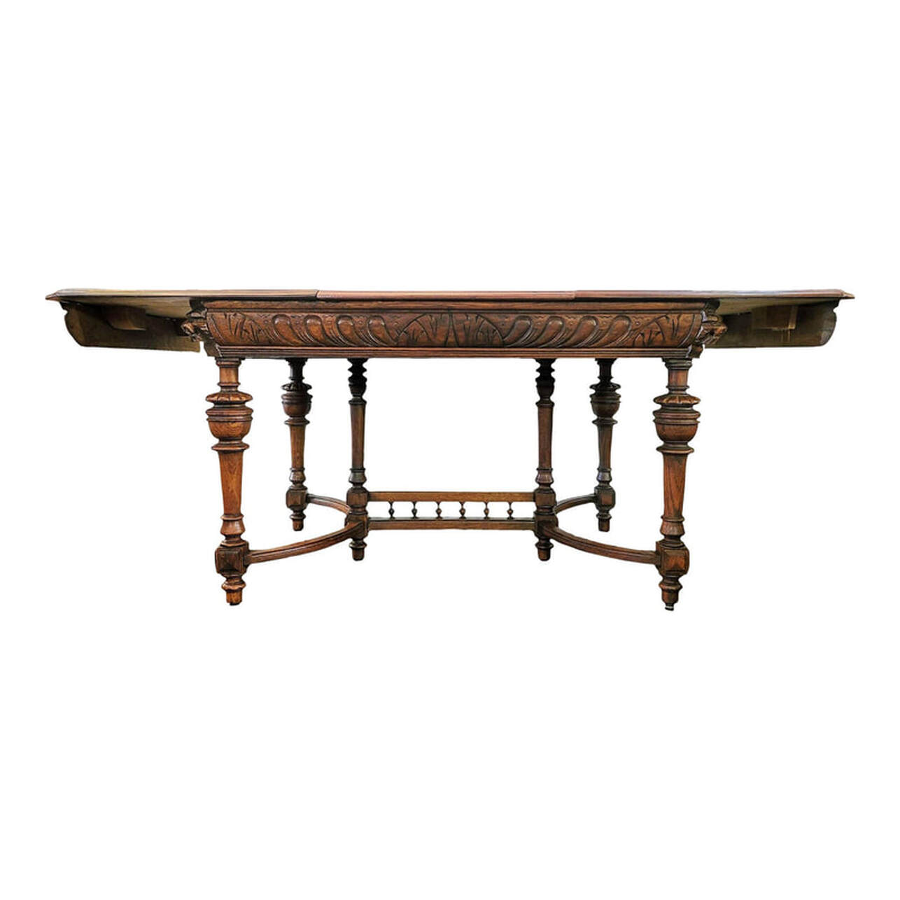 Well-crafted, beautiful, and sturdy carved oak dining table made in Mechelen, Antwerp, Belgium, circa 1900.  The closed table top is built from quarter-sawn oak wood, sometimes called tiger oak for the golden rays in the figure. The table top shows a seam down the middle. This is where the two ends of the top open for leaf placement. The table top edges are molded and match the molding on the ends of the table leaf. The corners are canted.  The table leaf is made from burl figure oak wood and has a finished molded edge to match the two halves of the table top. The leaf is placed in between the two halves of the table top to extend the length of the table. Underneath the center top on each side are round brass latches that lock the table top in place. We installed these latches. They easily unlatch to open the table for leaf placement. The steel plate at center is part of the old latching system and shows how a bar would have run through to hold the table top in place.  The table apron is embellished with carved arches and gadrooning with a molded bottom edge. The four canted corners are inset with carved blocks featuring projecting lion's heads. The holes through the mouths indicate the lion's heads once had hanging rings, a mask and handle motif dating back to ancient Rome and representative of strength, courage, and majesty.  The four oak corner legs and the two center legs are tapered over square blocks embellished with layered geometrics, turned, ringed, and carved, and end in turned, ringed arrow feet.  The Flemish style curved stretchers on each end attach to the square blocks on the legs.  The trestle is set between the two center legs and features a gallery of six turned wood Greek urn or amphorae shaped elements.  SIZE:  CLOSED:  50