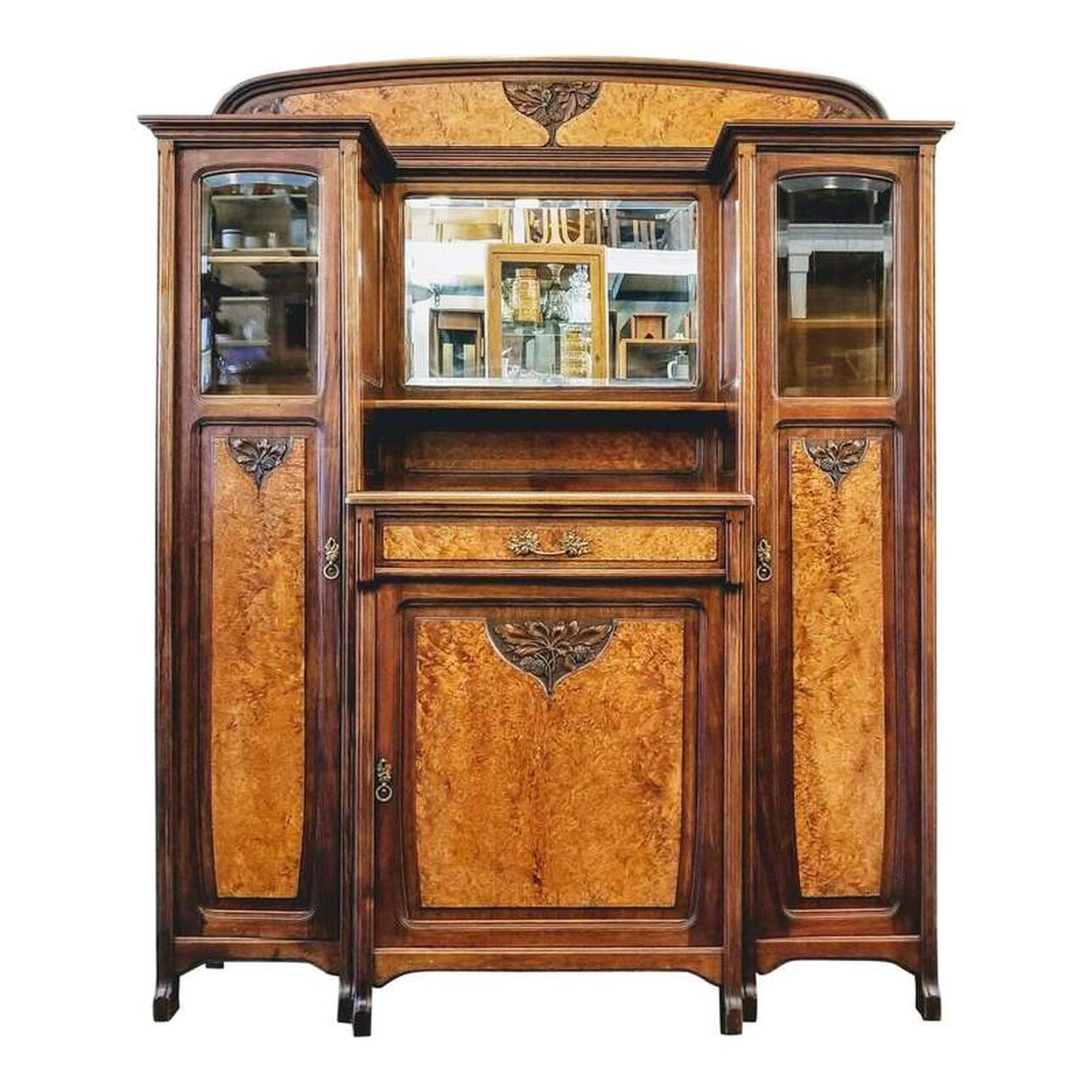 The main buffet featured here would have been designed and manufactured between about 1904 and 1906. The carcase is of the local antediluvian oak that Gauthier utilized with cupboard door fronts in a burry cut.  The pulls are in gilded bronze and designed to match the carved motifs based on natural elements, distinct clues of a Gauthier design influenced by the Nancy School.  Other features include a beveled mirror at center, beveled glass windows on each of the side doors, and adjustable shelves in the storage cabinets.