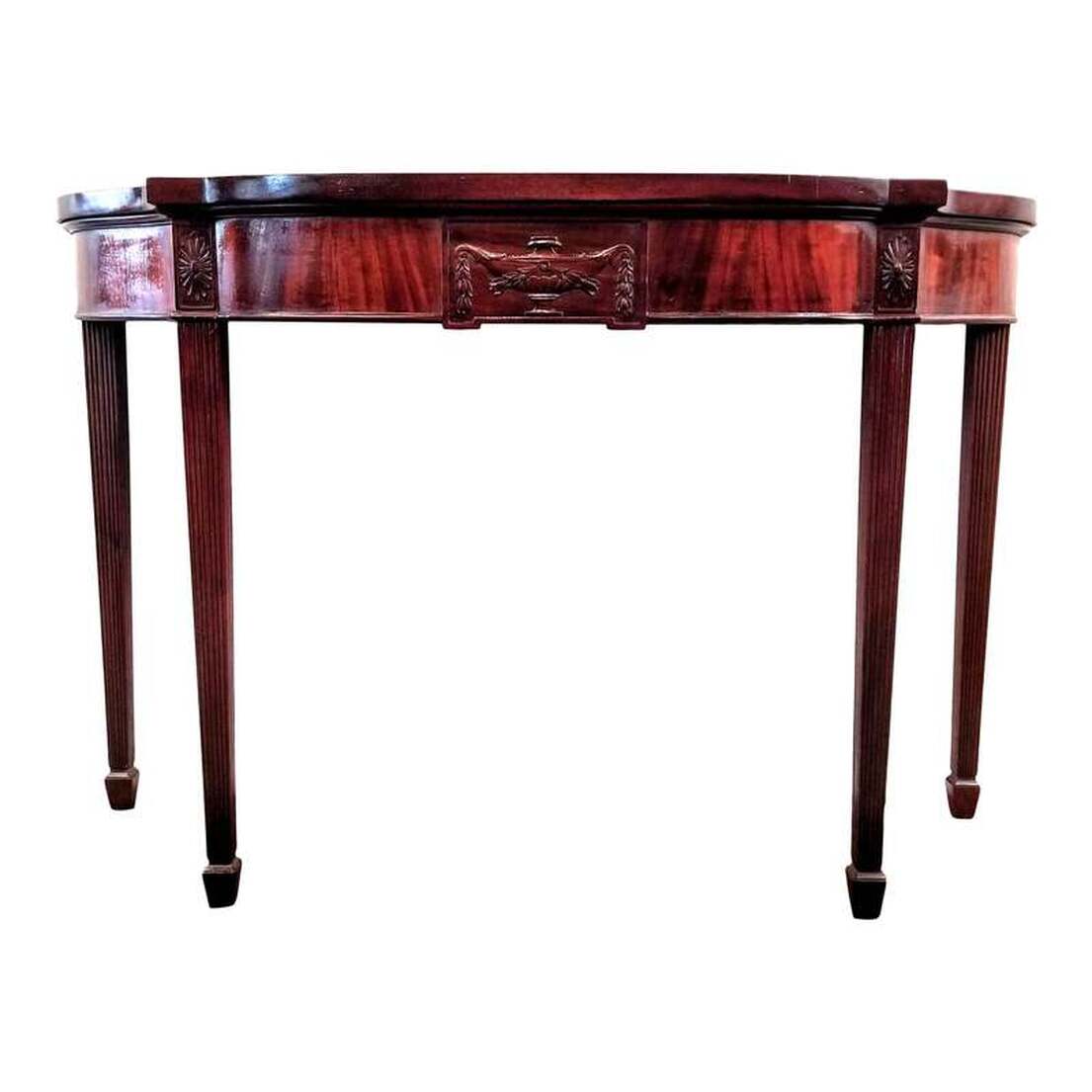 Vintage 1920s-1940s American made mahogany console table may be used also as a pier table, writing desk, serving table, entry hall table, and butler's table.  The style is in that of George III, with a shaped top, reeded and tapered legs, and a Neoclassical urn motif at front.  Table will complement rooms containing style elements of Adam, Georgian, Sheraton, Federal, Hepplewhite, and Phyfe.  Size :  48