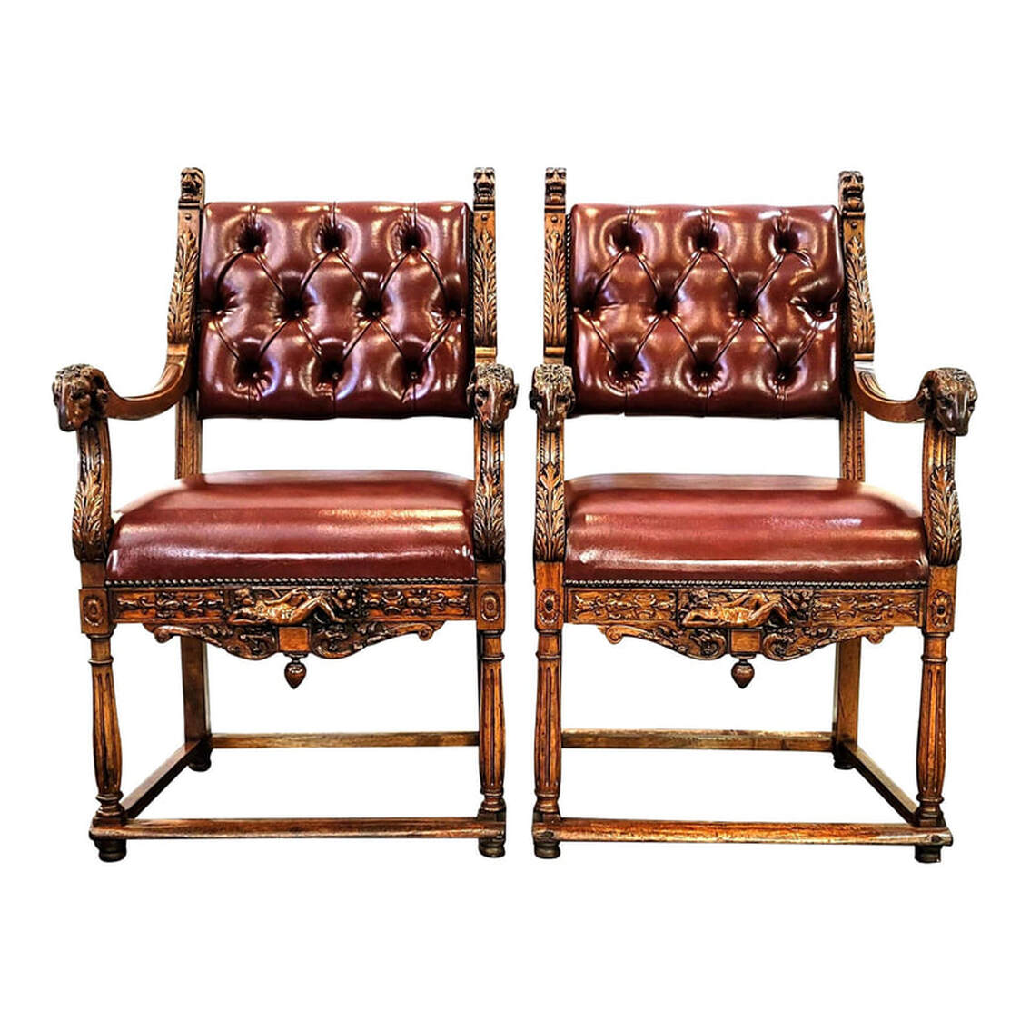 Pair late-19th-century through 1910 walnut French Renaissance Revival armchairs feature carvings of acanthus leaves, lion head finials, ram's heads at the ends of the arms, a nude reclining Demeter with cornucopia at the center of the front seat rails, and stylized scrolling dragons on the front aprons.  The backs and seats are upholstered in leather-like burgundy fabric with button tufting on the backrests.  Four low stretchers connect the legs above padded feet.