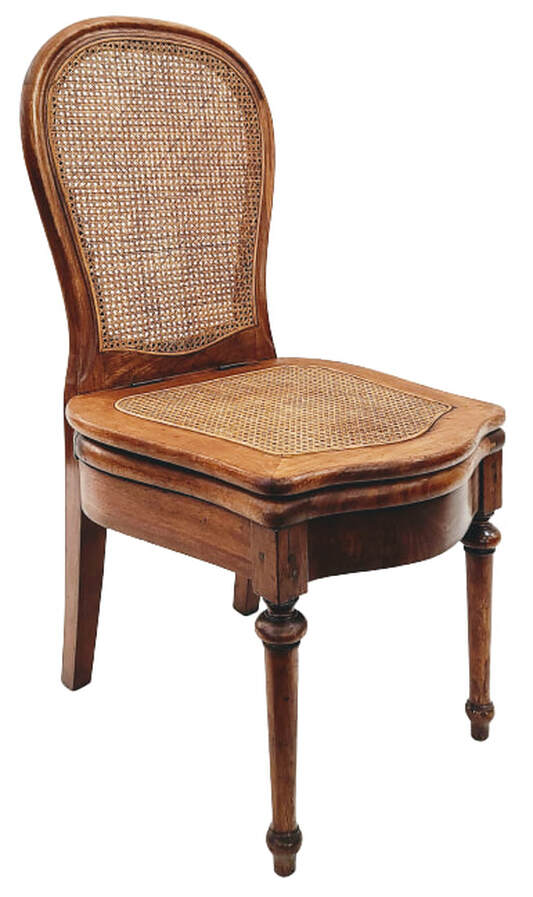 Mid-19th-century French double caned cherry wood commode chair / chaise percée / chaise nécessaire.  This style of commode chair was in use approximately from the time of Louis XIV through the 1920s. This chair was manufactured in the mid-1800s, during the reigns of King Louis-Philippe, followed by Emperor Napoleon III over France and of Queen Victoria over Great Britain.  The chair has a caned cartouche back, a caned curved top seat, an elegantly shaped open toilet seat, iron hinges, rear stiles ending in sabre legs, curved front and side seat rails, and ringed and tapered front legs under blocks.  The chair was constructed using various joinery techniques including pegs, mortise-and-tenon, and screws.  Chair may be installed in a powder room, boudoir, dining room, entry hall, or any space you require a useful conversation piece.  Chair will be a comfortable addition to interiors incorporating elements of style such as French Provincial, French Country, Louis XVI, Louis XV, Louis-Philippe, Edwardian, and Victorian.  SIZE:  19