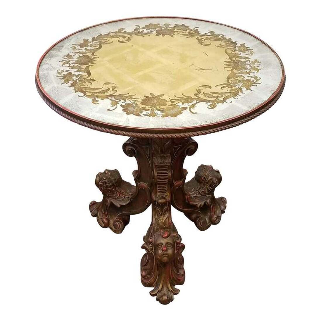 Round Italian center table with ornately carved gilt wood tripod base features putti heads and highlighting with red paint. At the top of the baluster stem sits a hand crafted verre eglomise top gilded in silver and gold with etched and painted images.