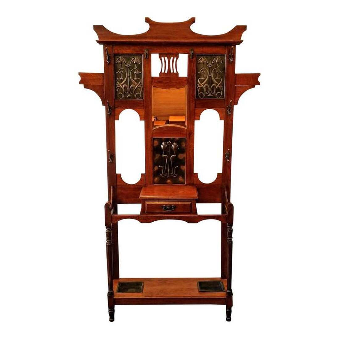 Shapland & Petter Ltd. of Barnstaple, North Devon, England Arts & Crafts oak hall stand features a central beveled mirror, two silvered copper repousse panels at top, and a copper repousse panel below the mirror. The repousse panels feature Arts & Crafts tulip motifs. A single drawer offers storage for your keys and change as you walk in the door. The iron hooks are all marked with registered design number 535663, which places the date for their initial manufacture as 1909-1910. Metal inserts at the base provide storage for umbrellas, parasols, canes, walking sticks, and swagger sticks. S&P gave this model the