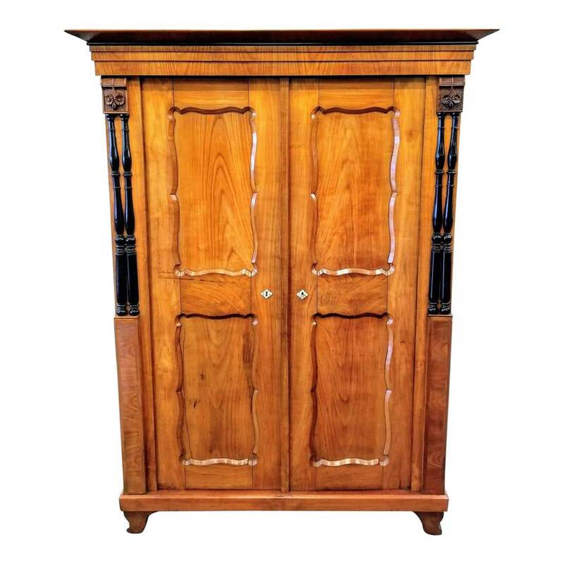 Biedermeier style armoire / linen press / wardrobe from circa the 1830s is constructed of hand-planed cherry wood. Adding interest are two carved bone key escutcheons, central stringing inlay, ebonized balusters, and carved floral applications.