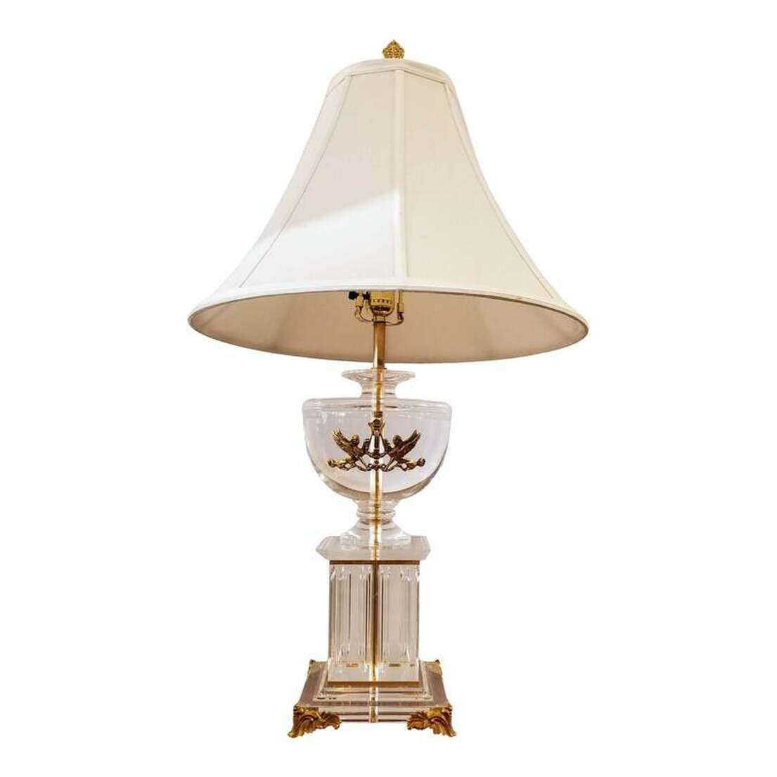 Neoclassic style table lamp in the form of a fluted column pedestal on gilt acanthus scroll feet surmounted by a lebes urn fronted with a gilt pair of sphinx on either side of a lyre.  The base material is clear acrylic thermoplastic resin, known by the trade name Lucite.  The brass spacers and hardware are brass.  The light turns on via a 3-way rotary lamp switch.
