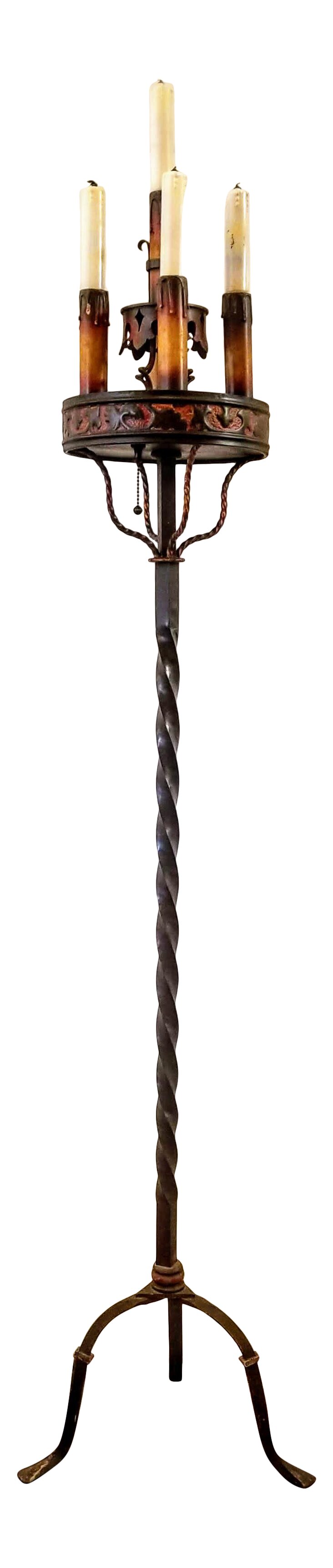 Bring an element of Old World Charm into your space with this vintage late-1920s to early-1930s Spanish Colonial Revival Monterey style wrought iron floor lamp torchiere.  The fish-tail foot tripod base supports a vertical black wrought iron twist topped with four brass-tone twists crowned with a polychromed round on which sit a candelabra of five polychromed bulb insets. The painted glass bulbs are in the shape of dripping pillar candles with black wicks.  The hand-forged and blacksmith-worked iron guarantees enduring quality.  The electric lamp is in working order. A chain pull turns on the light bulbs.